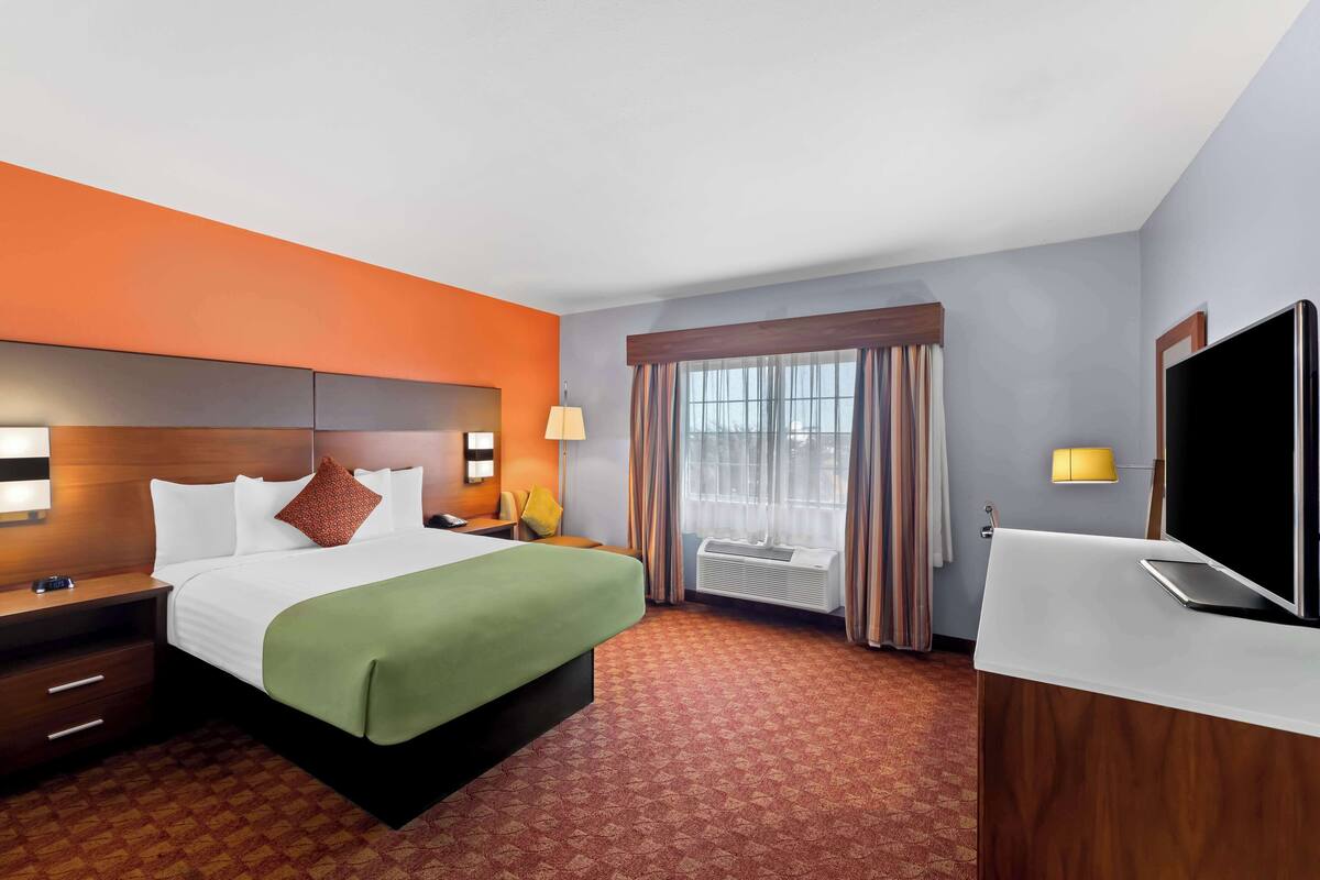 A hotel room with a bed, a desk, a TV, and a window with curtains.