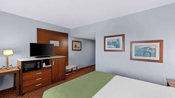 A hotel room with a bed, a TV, a microwave, a small table, and framed pictures on the wall.