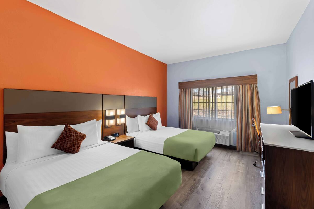 A hotel room with two beds, a desk, a TV, and a window with curtains.