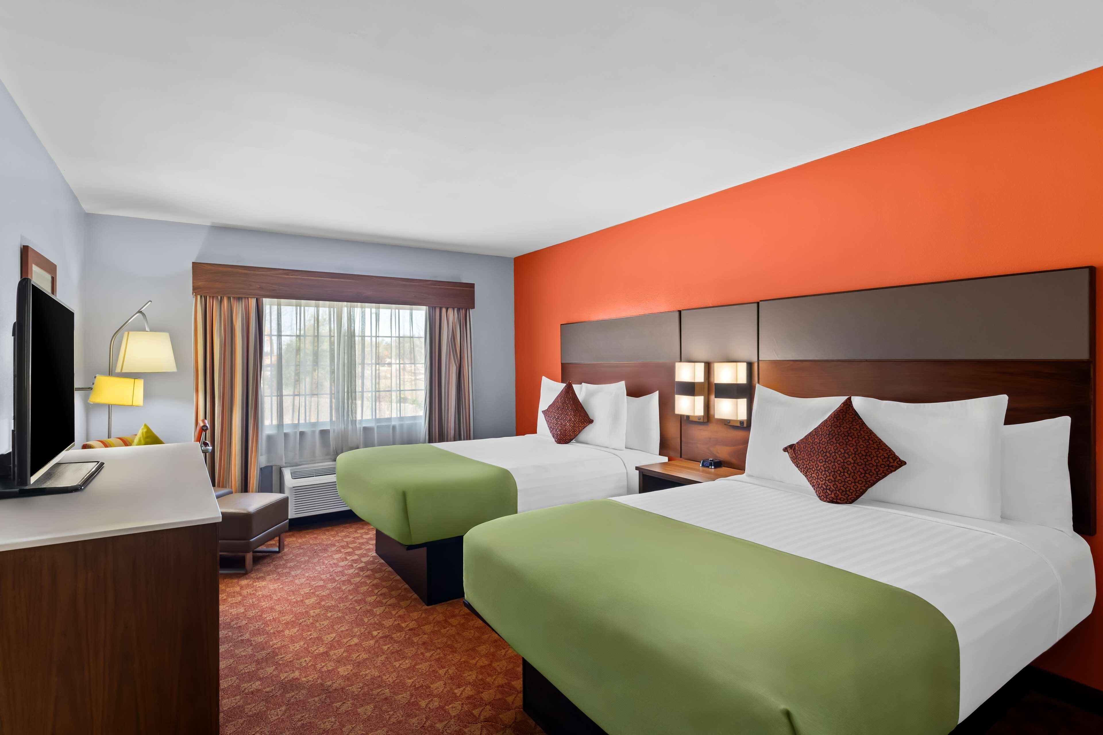 Ein Hotelzimmer mit zwei Betten, einem Schreibtisch, einem Fernseher und einem fenster mit Vorhängen.