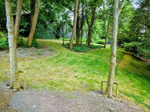 Un jardín ajardinado con árboles, césped y un banco de madera.