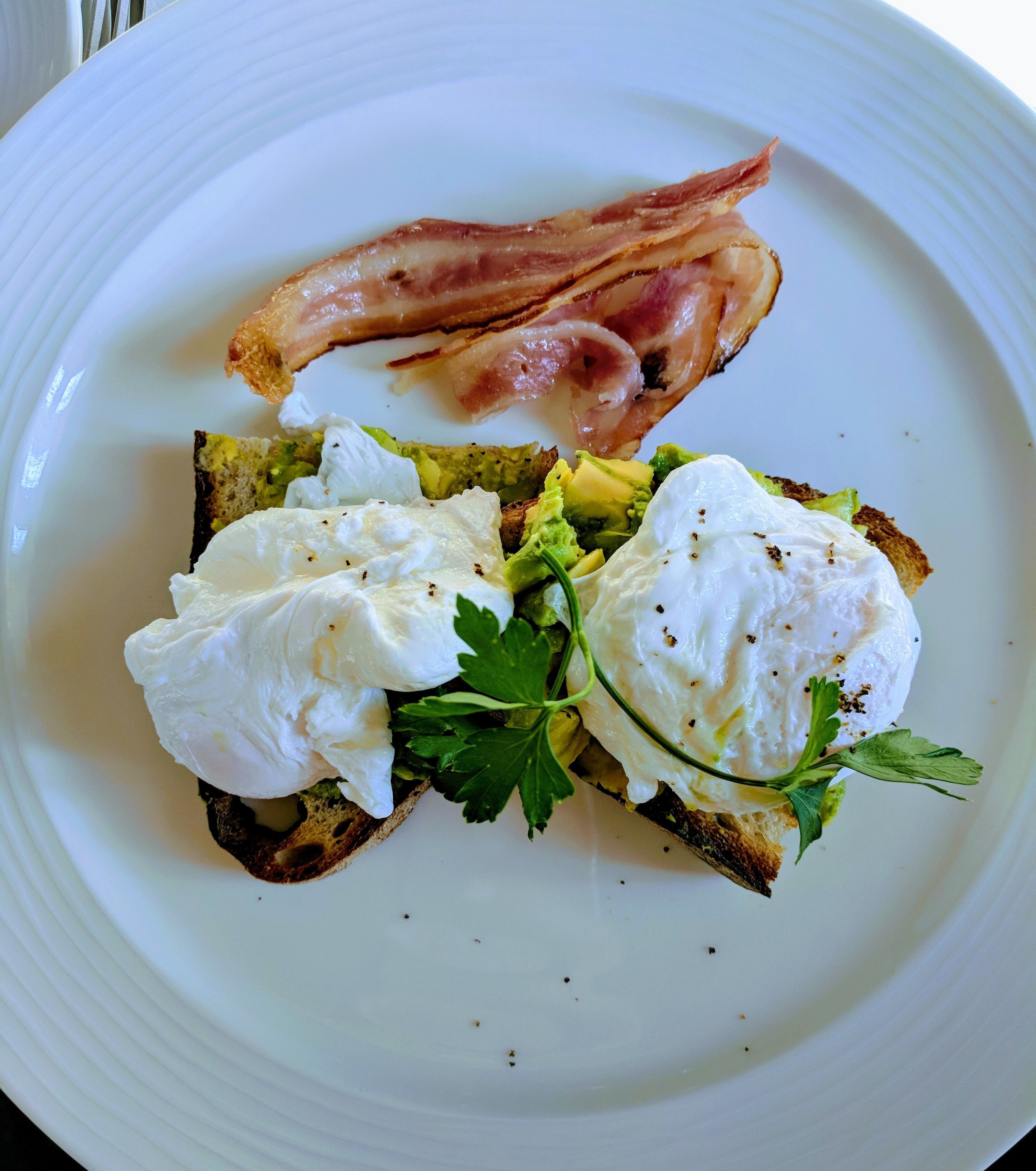 Une assiette avec des tranches de pain grillé garnies d’avocat, d’œufs pochés et de bacon.