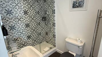 A bathroom with a shower, toilet, sink, and a patterned wall.