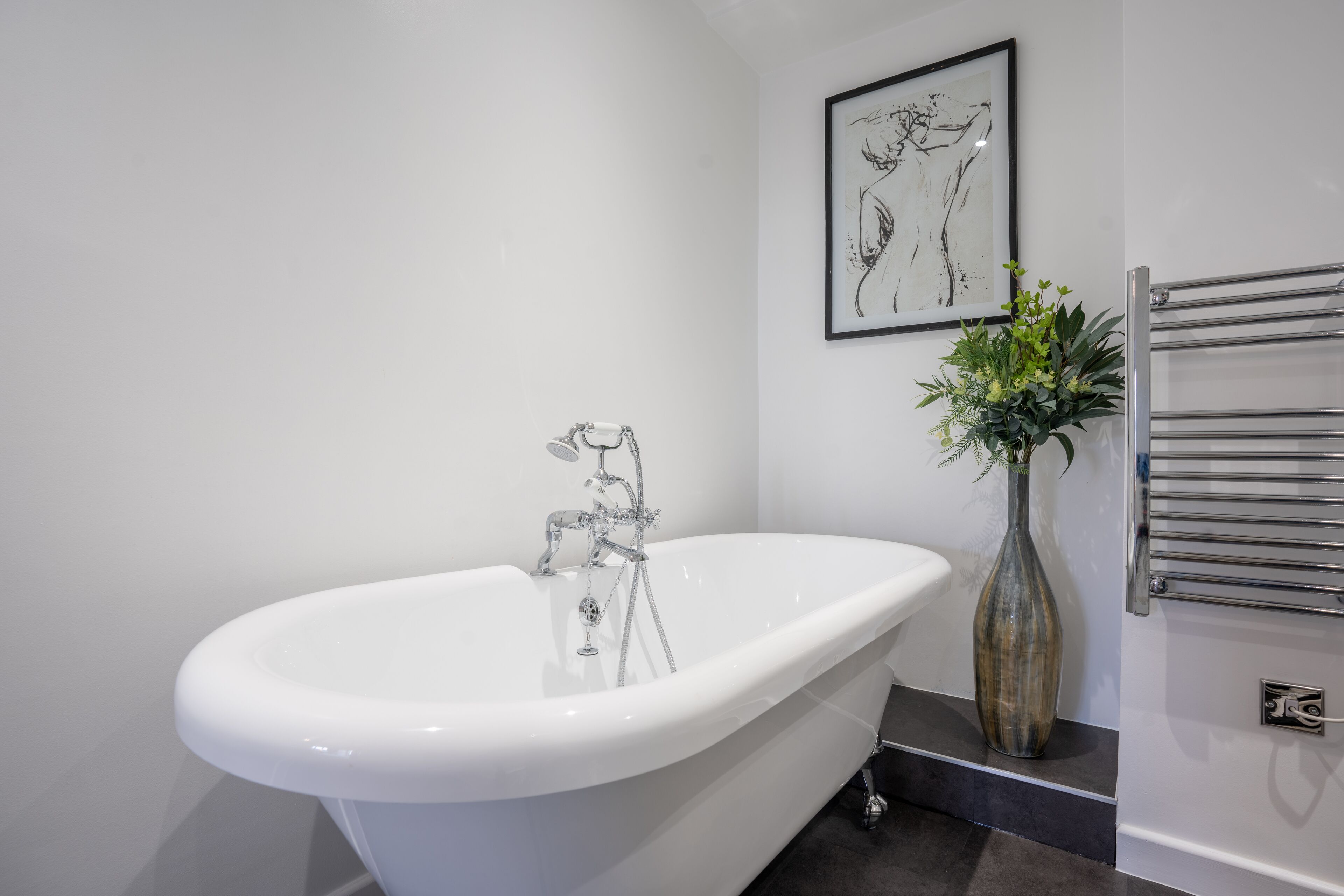 A modern bathroom with a freestanding bathtub, a wall-mounted towel rack, and a framed artwork above the tub.
