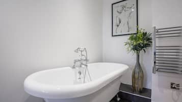 A modern bathroom with a freestanding bathtub, a wall-mounted towel rack, and a framed artwork above the tub.
