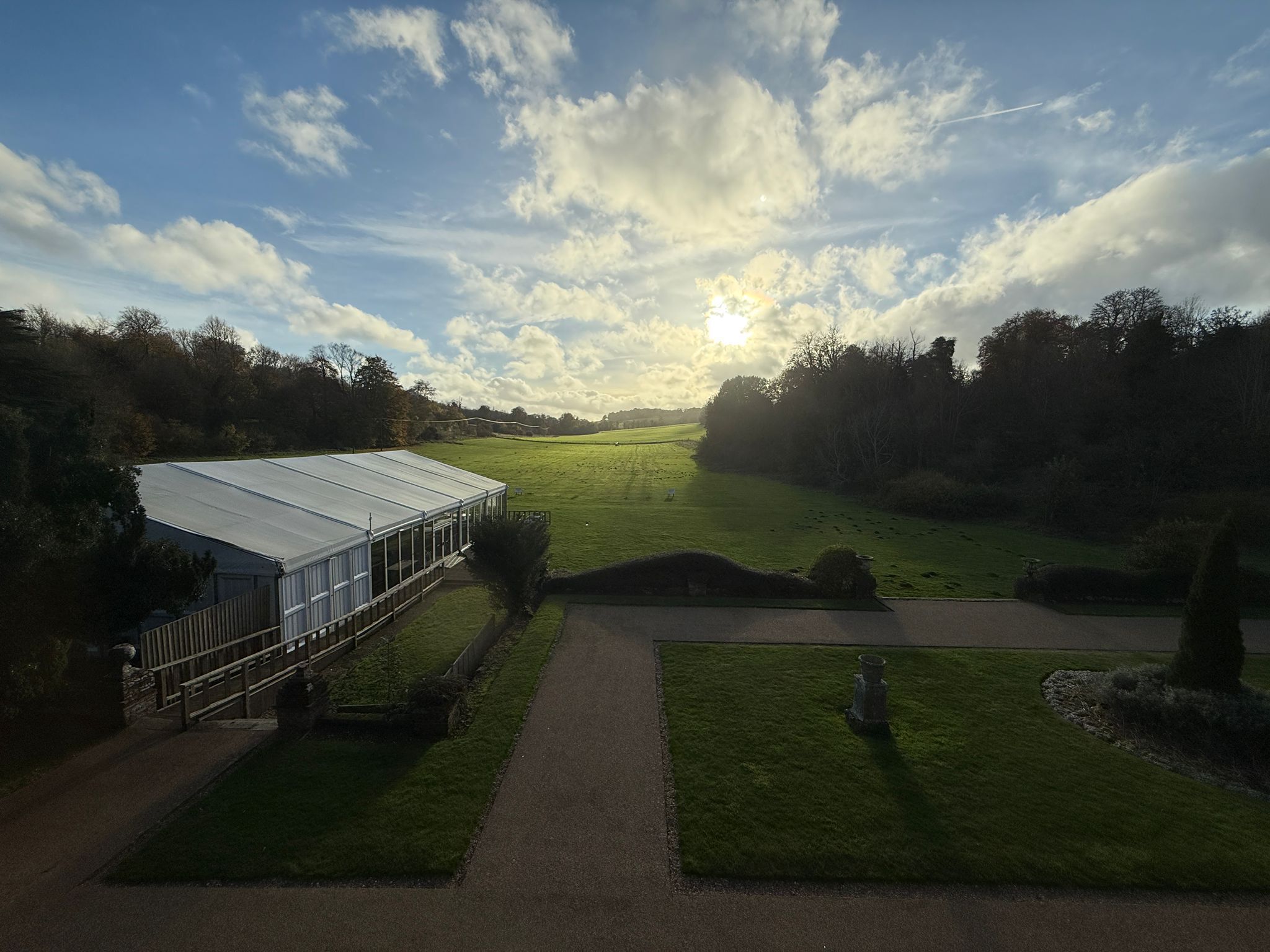 A greenhouse structure with a pathway leading to it, surrounded by a grassy field and trees.