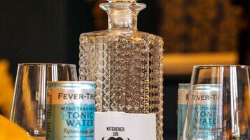 Ein Tisch mit einem Kristallkarafell, zwei Gläsern und zwei Dosen Fever-Tree Tonic Water. Außerdem ist ein Schild mit einem Schnurrbart-Design zu sehen.