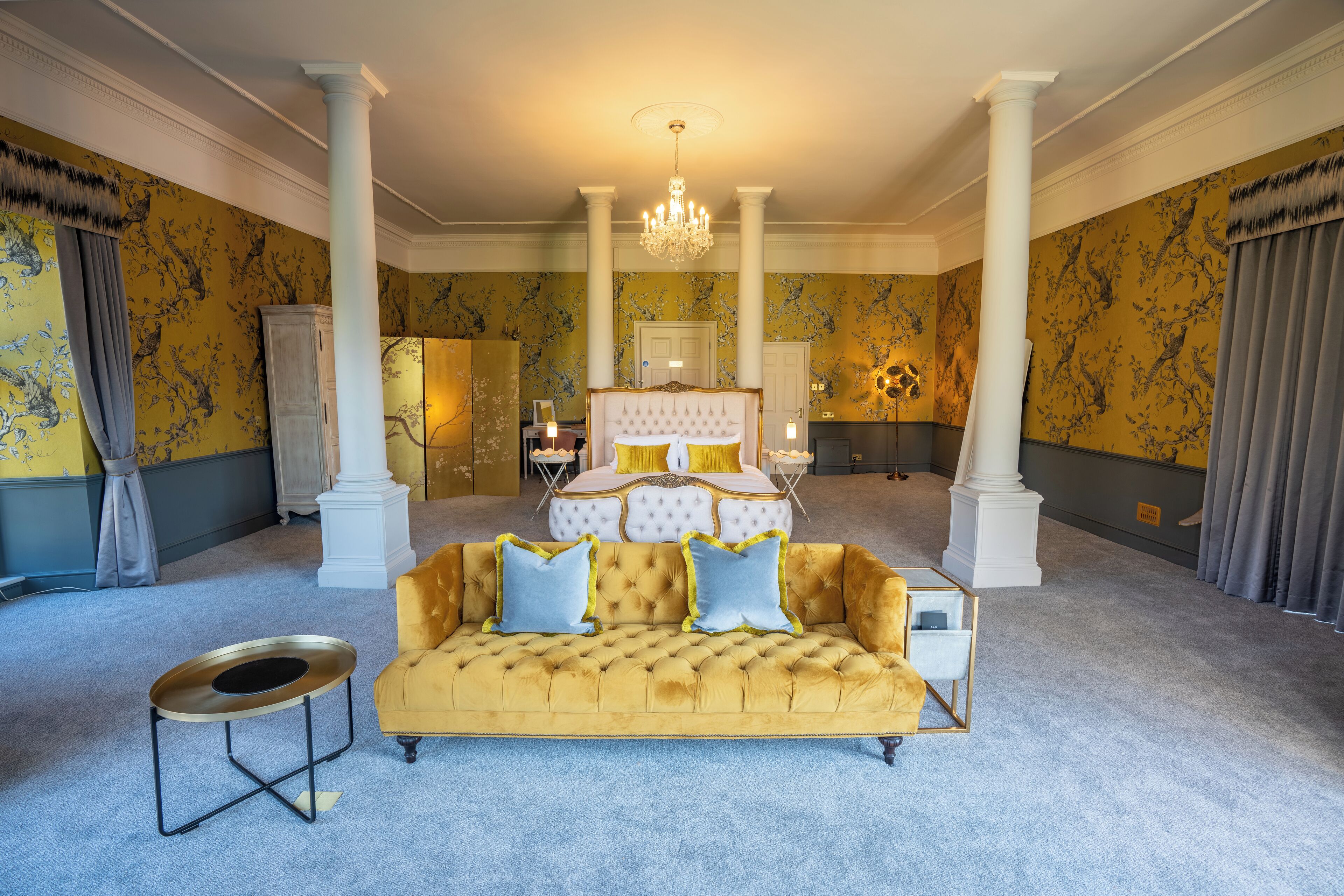 Une chambre à coucher luxueuse, dotée d’un grand lit, d’un canapé de couleur dorée et d’un lustre.