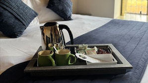 A neatly made bed with a tray of breakfast items, including green cups, a kettle, and packaged goods. - Broome Park Hotel (Canterbury)