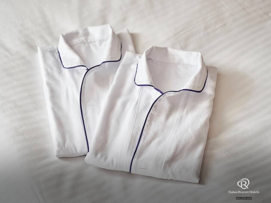 Two neatly folded white shirts with dark blue piping on a bed.