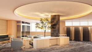 En moderne hotellobby med et centralt receptionsområde, siddepladser og et stort vindue der lukker naturligt lys ind.