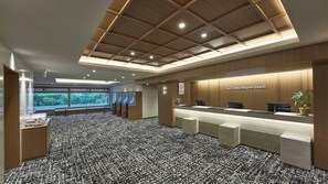 A hotel reception area with a reception desk, a large window offering a view of greenery, and a patterned carpet. - Daiwa Roynet Hotel Tokyo Osaki (Tokyo)