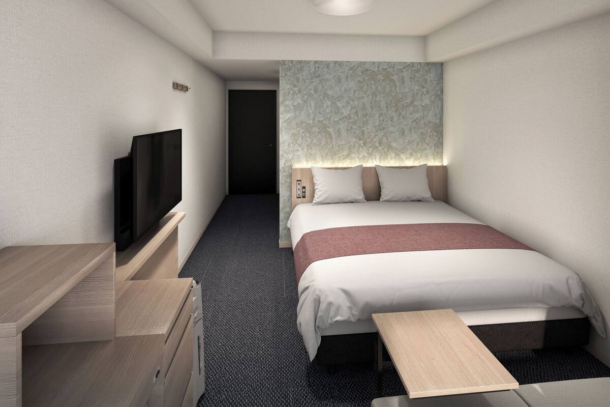 Une chambre d’hôtel avec un lit, une table de chevet, une télévision et un petit bureau.