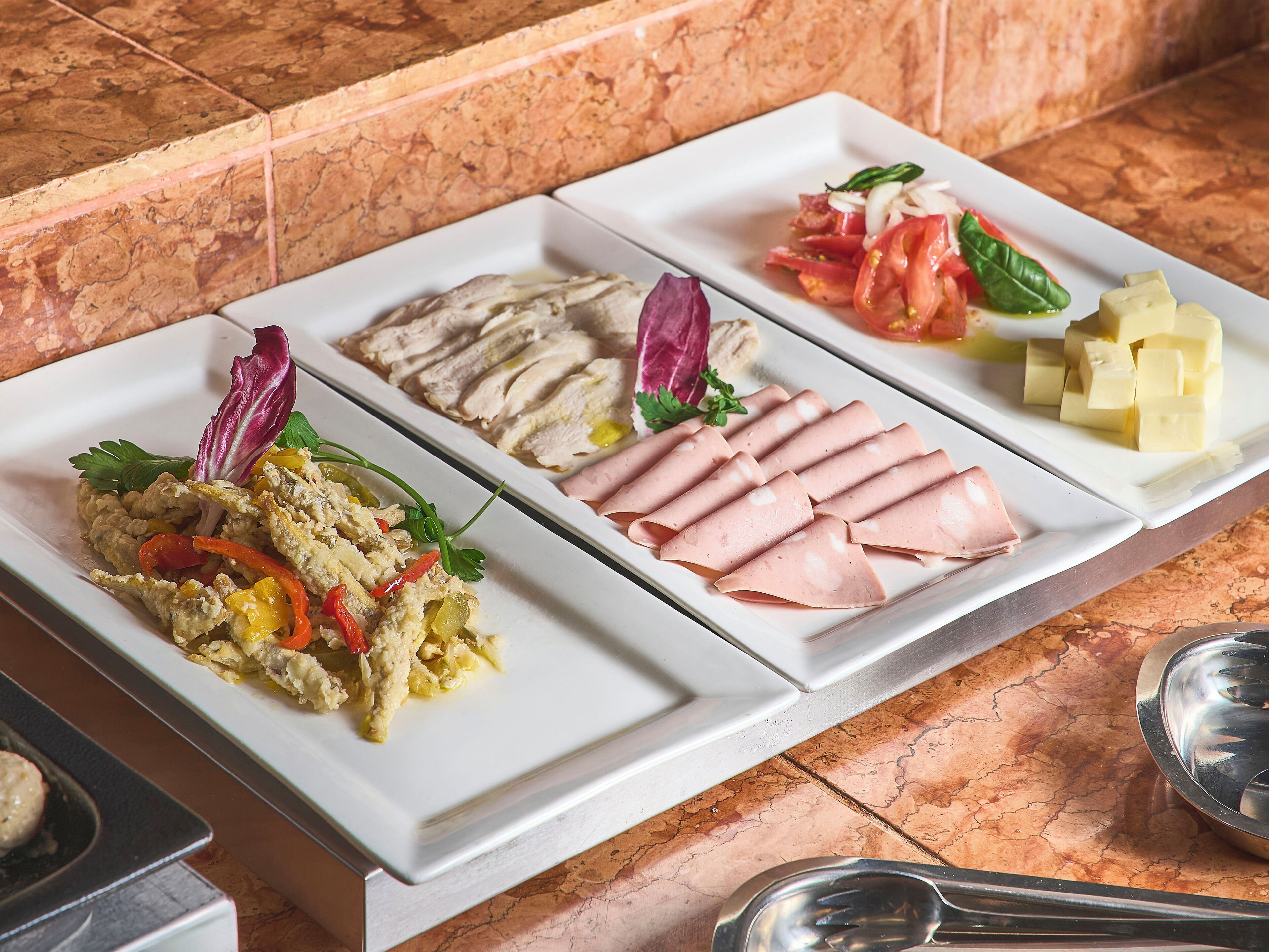 Un buffet con diversi piatti, tra cui uova strapazzate, prosciutto a fette e un'insalata con pomodori e formaggio.