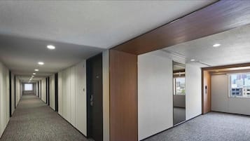 A hotel corridor with a carpeted floor, wooden paneling, and a city view through a window.