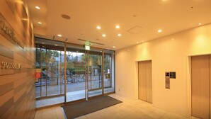 Un hall d’hôtel moderne avec des portes vitrées, un comptoir d’accueil et deux ascenseurs.