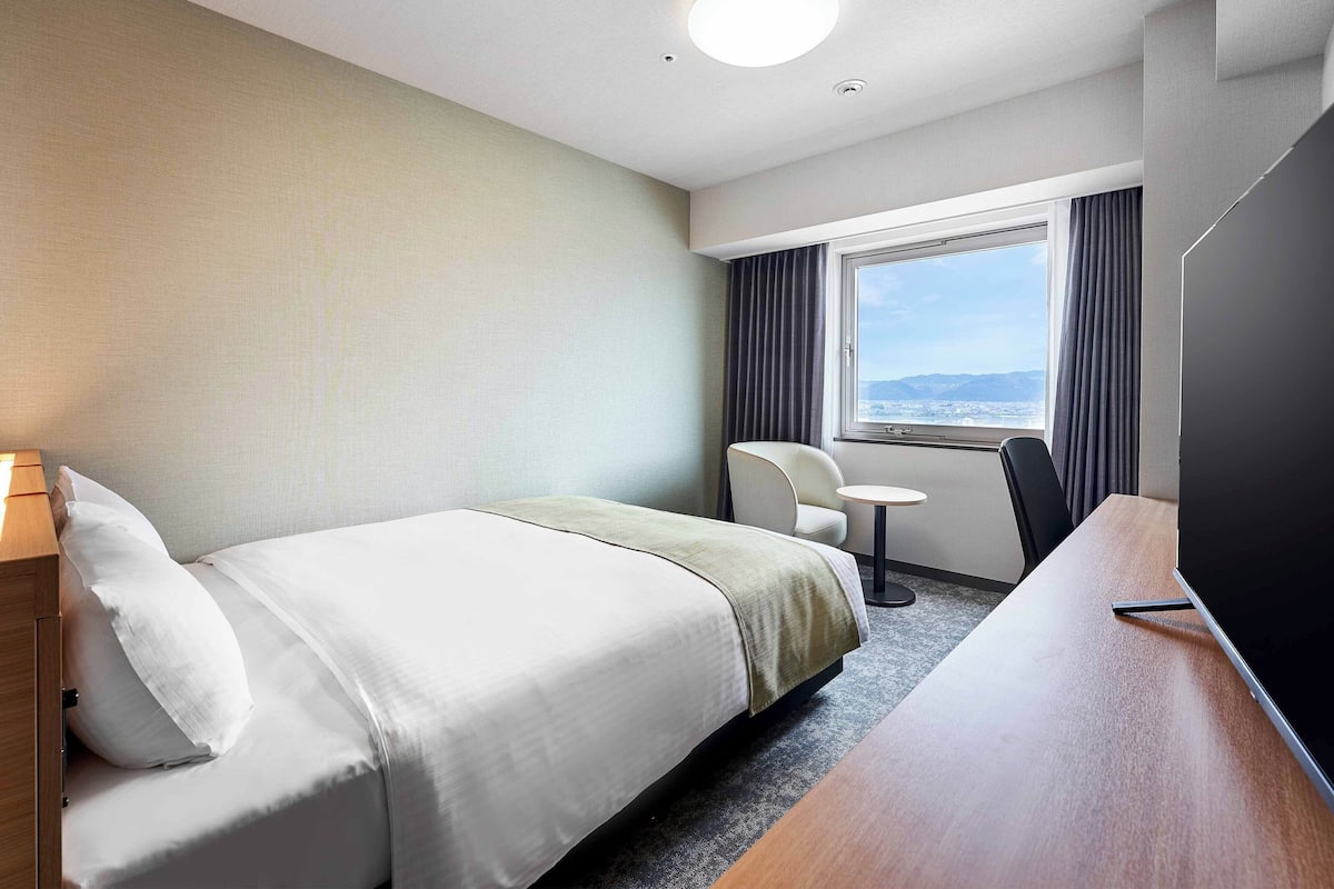 Ein Hotelzimmer mit Bett, Schreibtisch, Stuhl, Nachttisch und Fernseher.