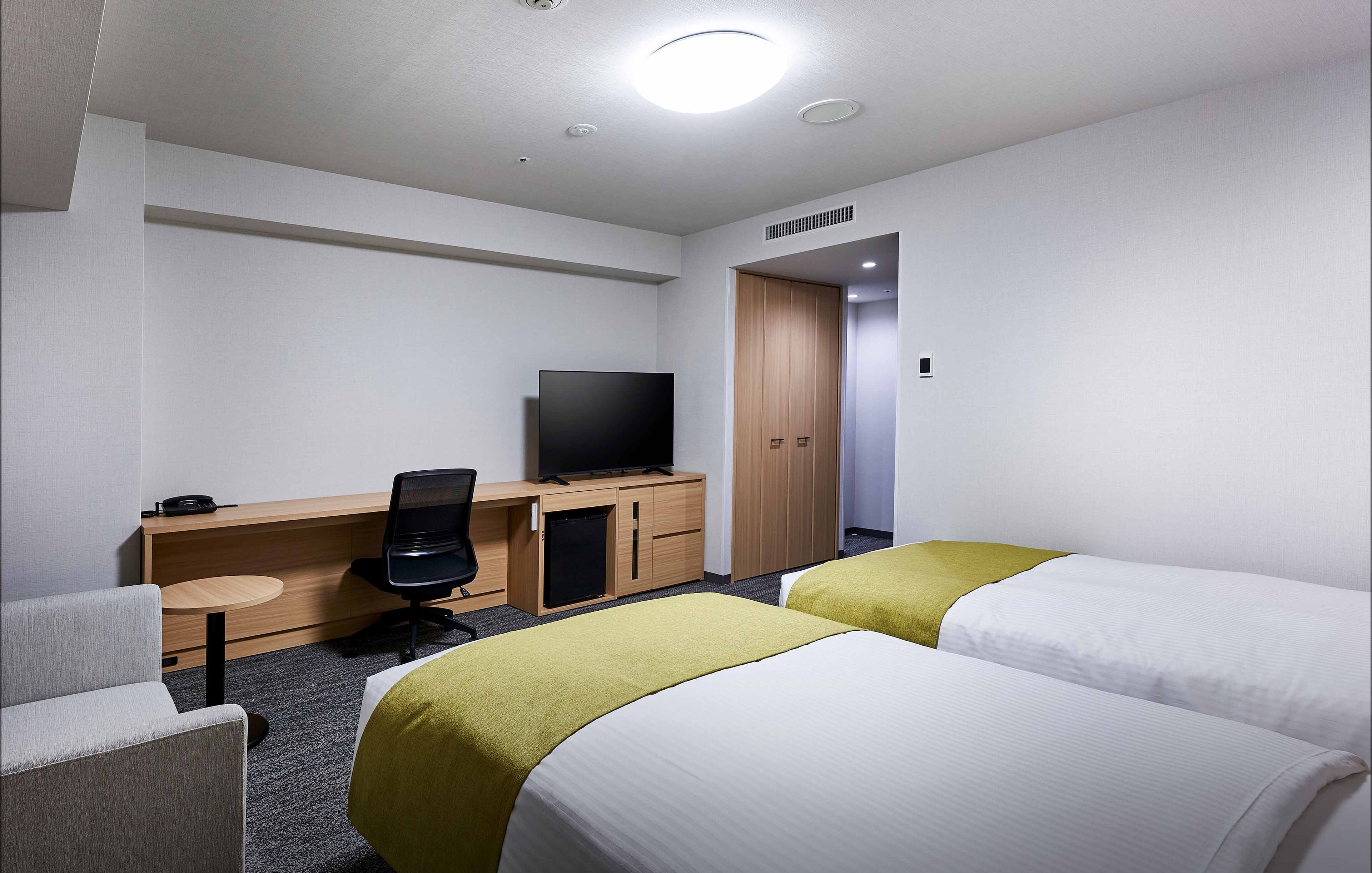 A hotel room with two beds, a desk with a television, a chair, and a small table.