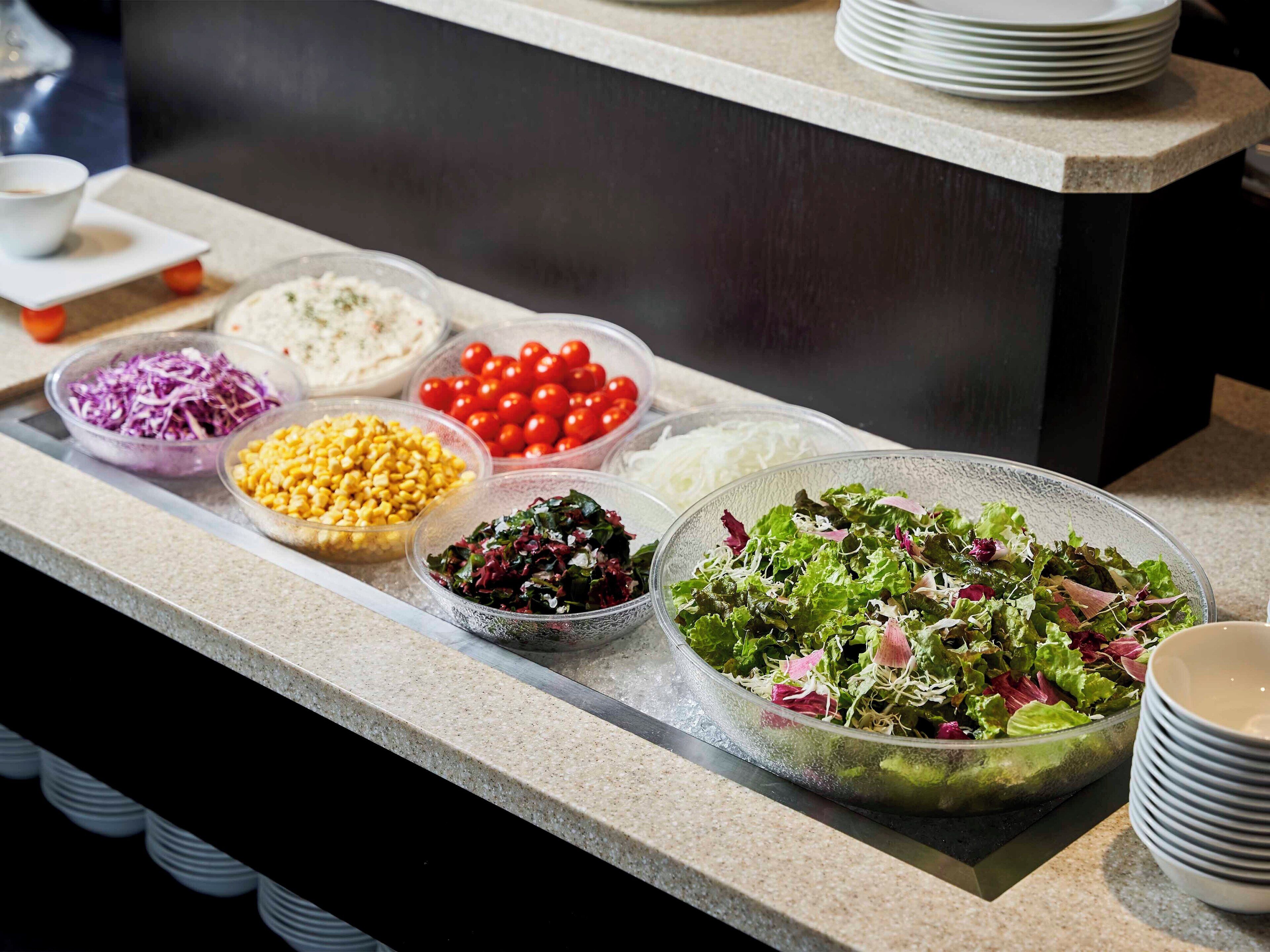 A buffet with various food items including salads, vegetables, and corn.