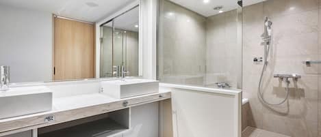 A modern bathroom with a large mirror, two sinks, a shower, and a vanity with storage.