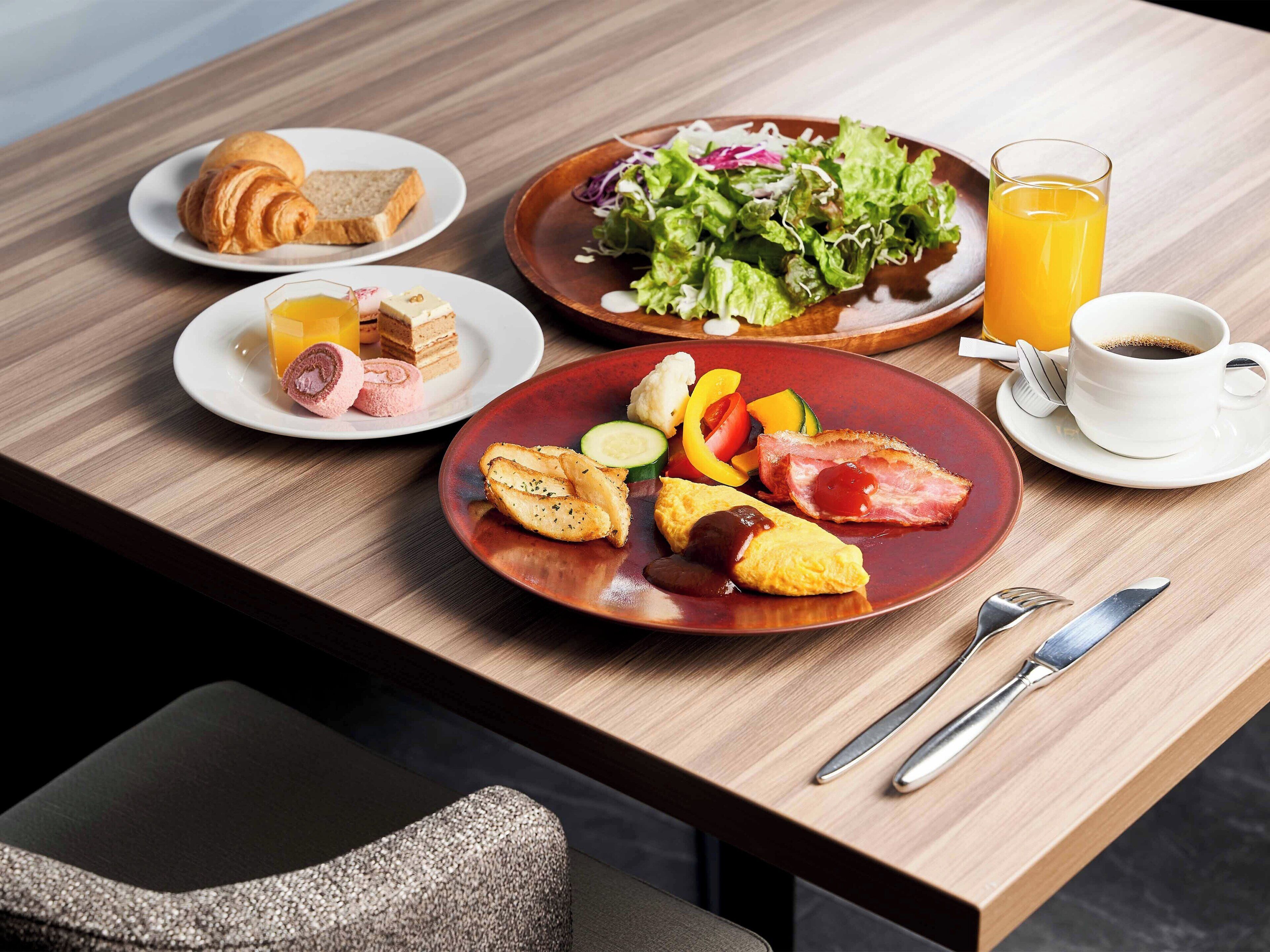 A breakfast table with croissants, a plate of eggs, a salad, and a glass of orange juice.