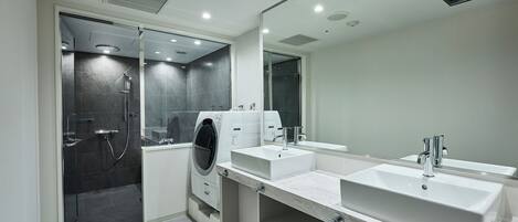 A modern bathroom with a glass shower enclosure, a built-in washing machine, and a large mirror above the sink.