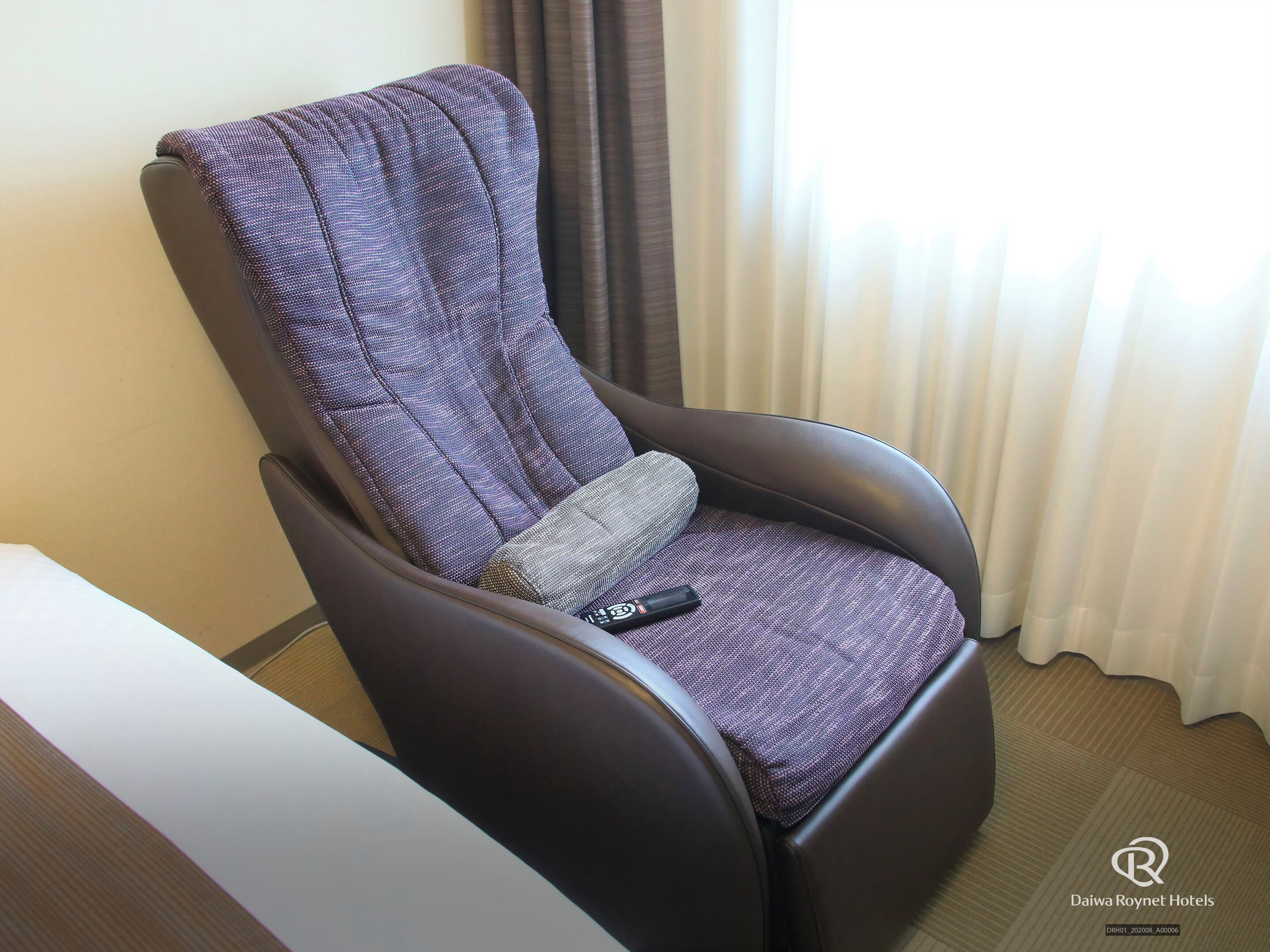 Uma poltrona reclinável com tecido estampado, um controle remoto no assento e o logotipo de Daiwa Roynet Hotels.