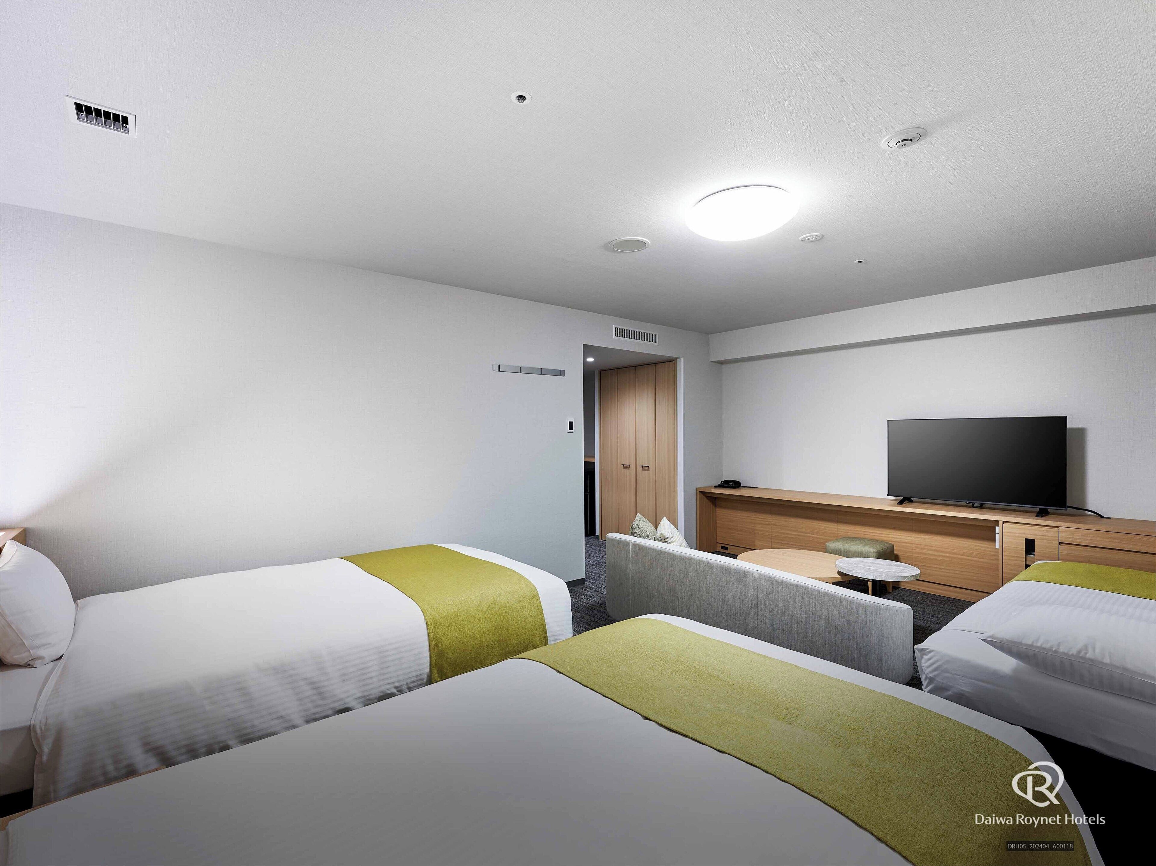 A hotel room with two single beds, a TV, a desk, and a wardrobe.