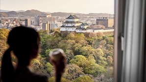 Une vue depuis la fenêtre d’une chambre d’hôtel, donnant sur l’architecture traditionnelle japonaise, le paysage urbain et une colline boisée.