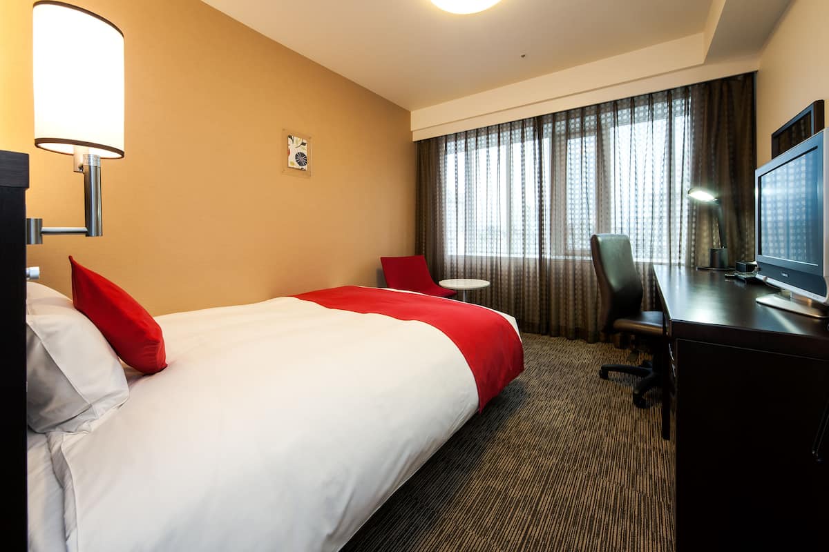 Une chambre d’hôtel avec un grand lit, un bureau avec un ordinateur, une chaise, une petite table et un téléviseur.