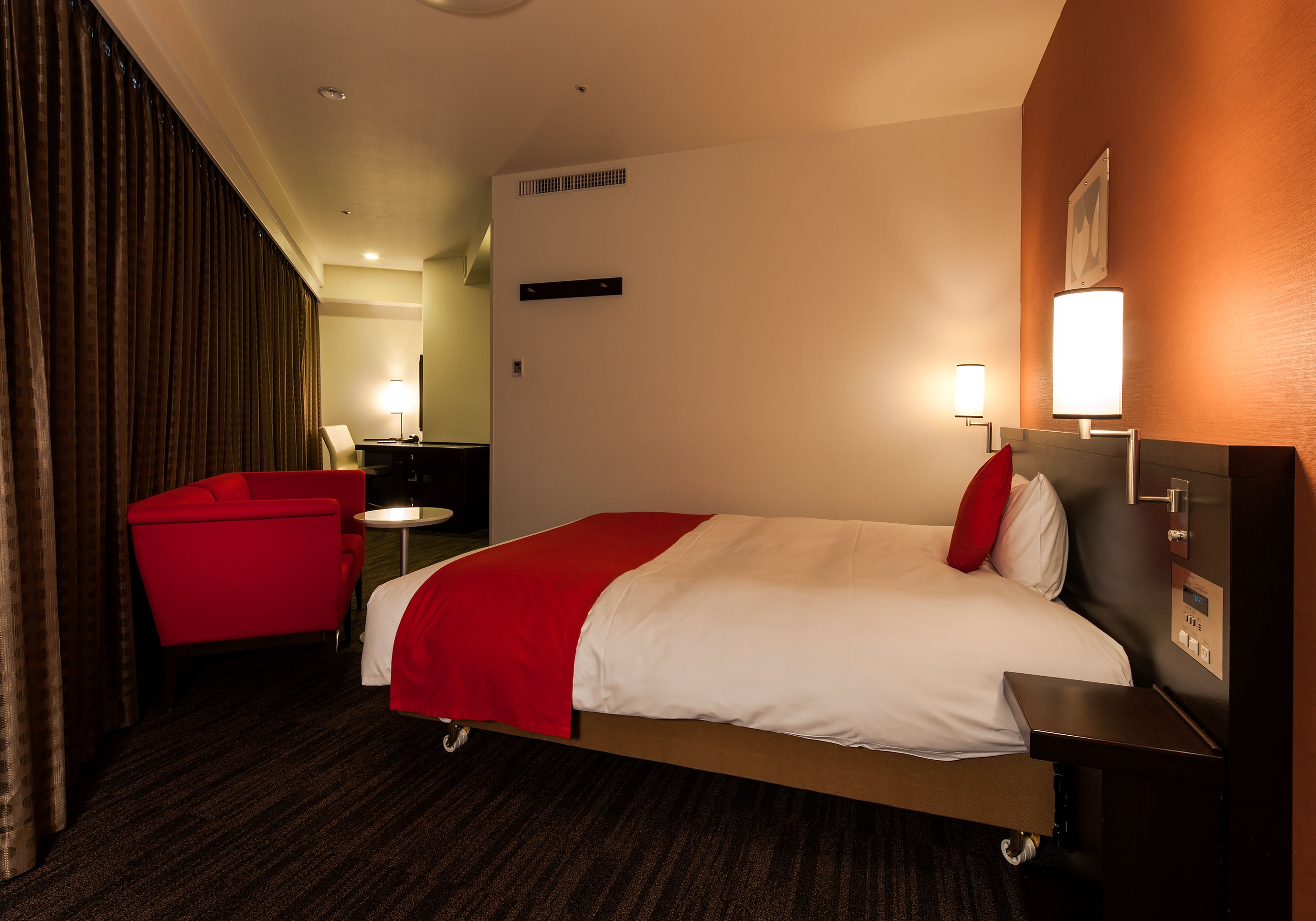 Una habitación de hotel con una cama, un sillón rojo, una mesita y una mesita de noche.