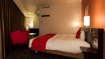 Una habitación de hotel con una cama, un sillón rojo, una mesita y una mesita de noche.