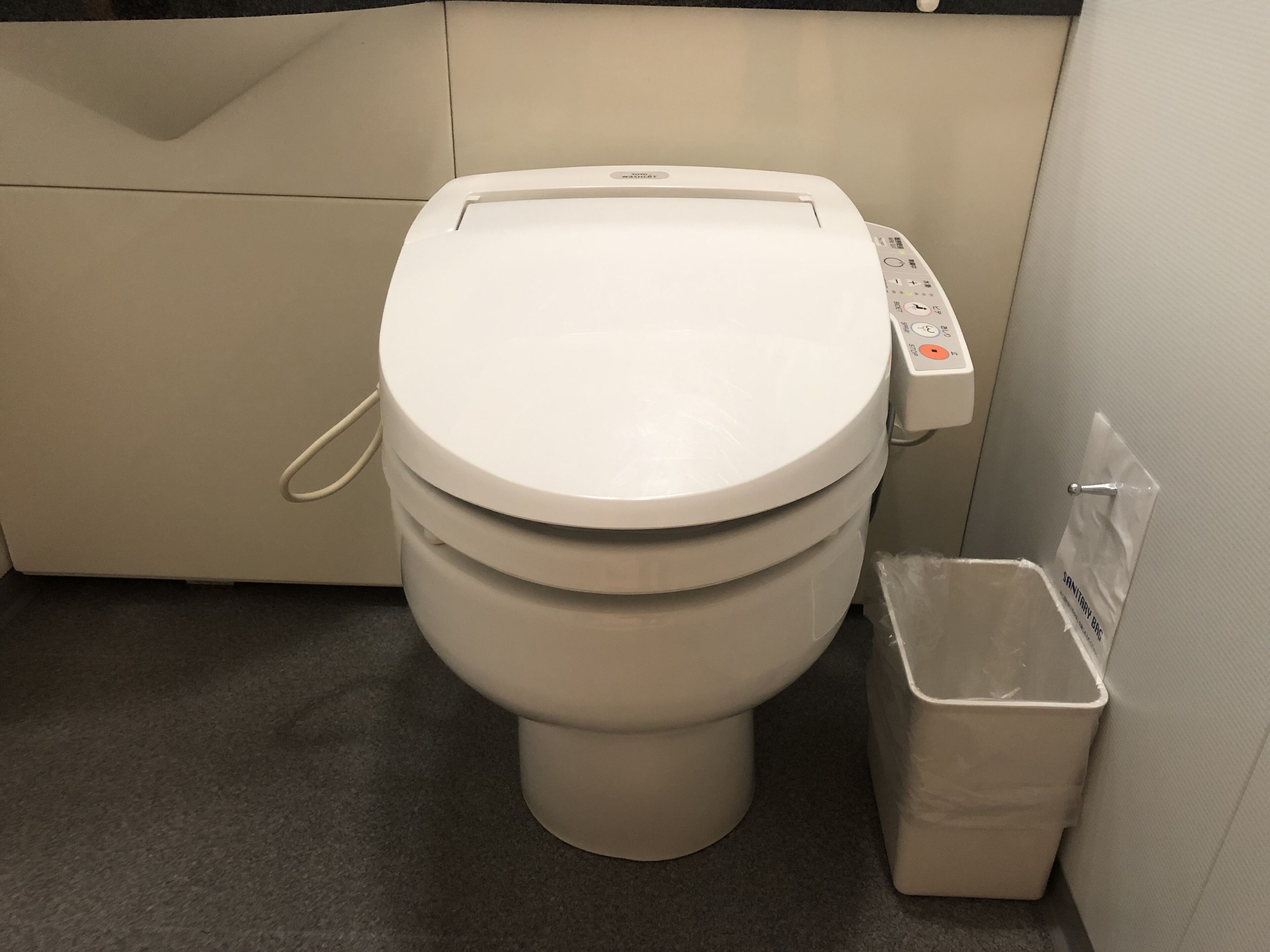 A toilet with a control panel, a trash bin, and a tiled wall.