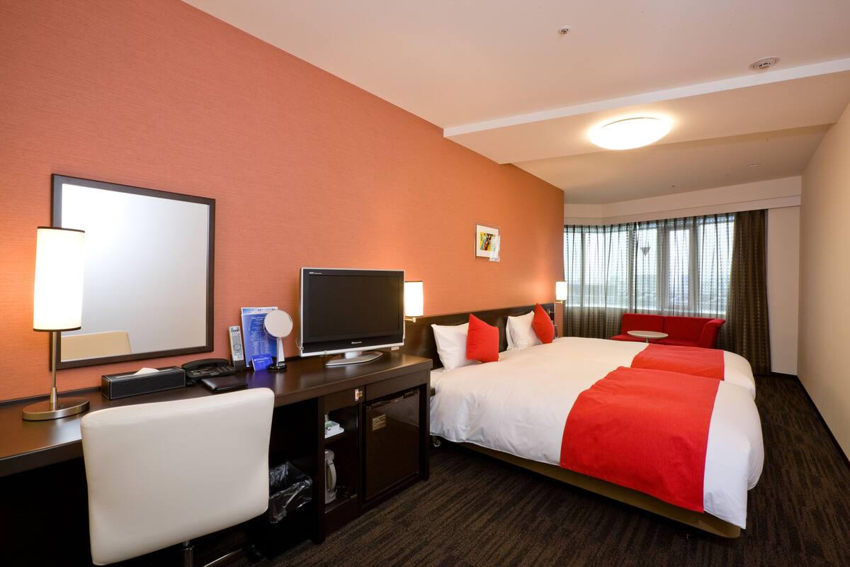 Une chambre d’hôtel avec un grand lit, un bureau avec une télévision, une chaise et un petit bureau avec une lampe.