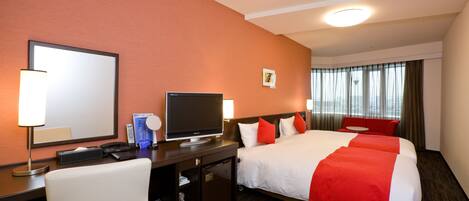 A hotel room with a large bed, a desk with a television, a chair, and a small desk with a lamp.