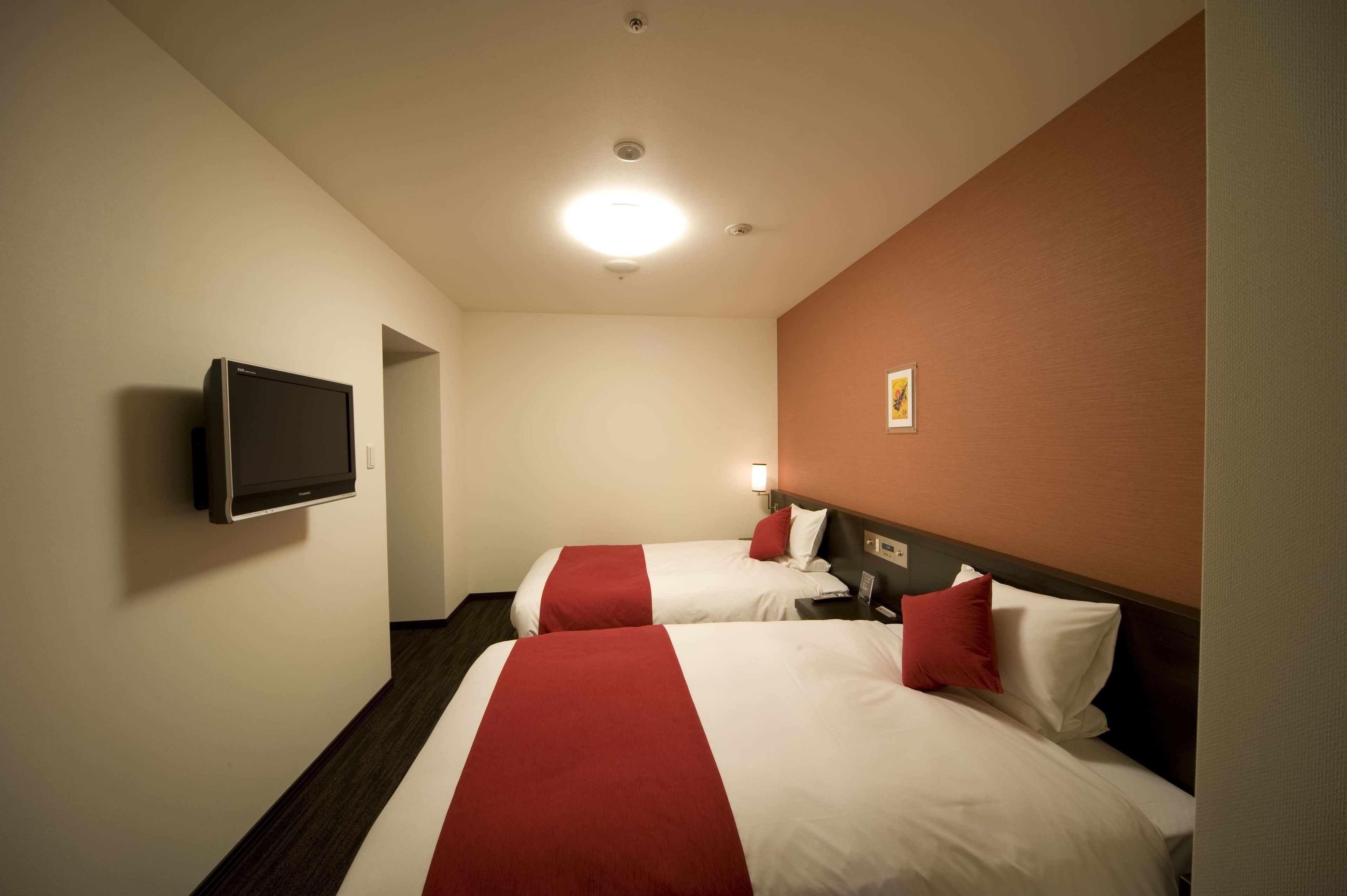 Quarto de hotel com duas camas, uma televisão na parede e um pequeno quadro.