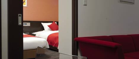 A hotel room with a bed, a red sofa, a white table, and a door leading to another room.