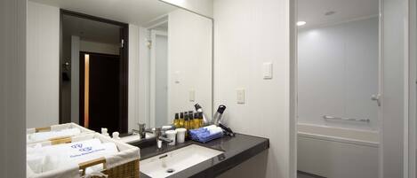 A modern bathroom with a large mirror, a white sink, and a black countertop. There is a wicker basket with towels and toiletries on the sink.