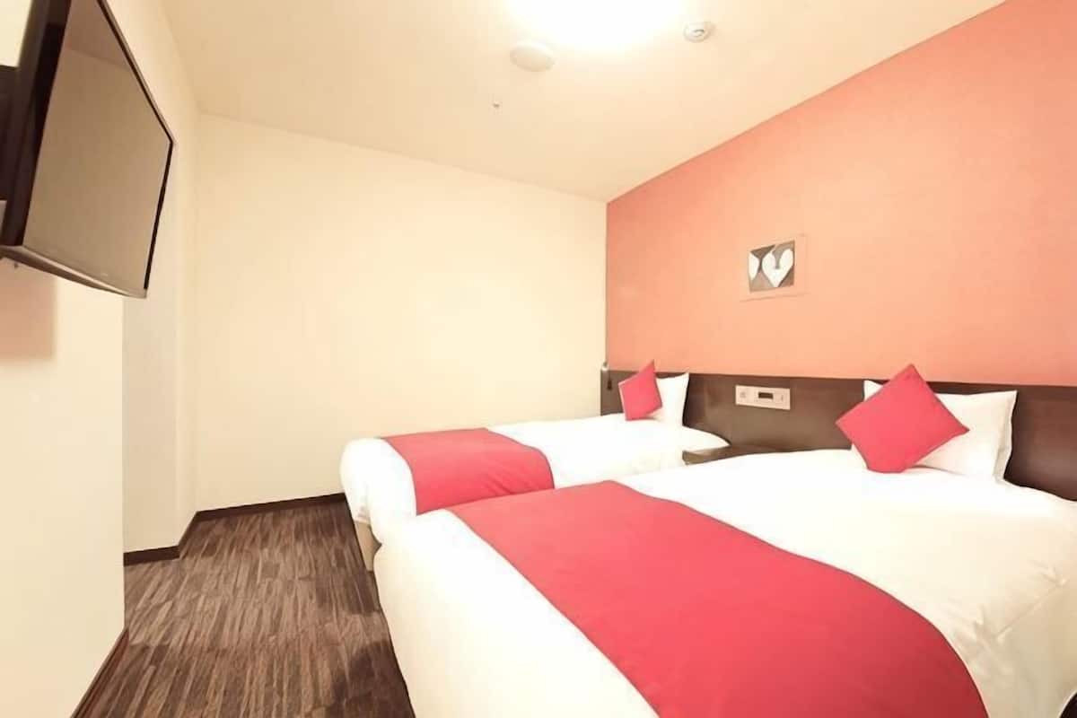 A hotel room with two beds, a flat-screen TV, and a wall-mounted light fixture.