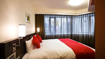 Une chambre d’hôtel avec un lit bien fait, une table de chevet avec une lampe, un panneau de commande fixé au mur et une fenêtre avec des rideaux.