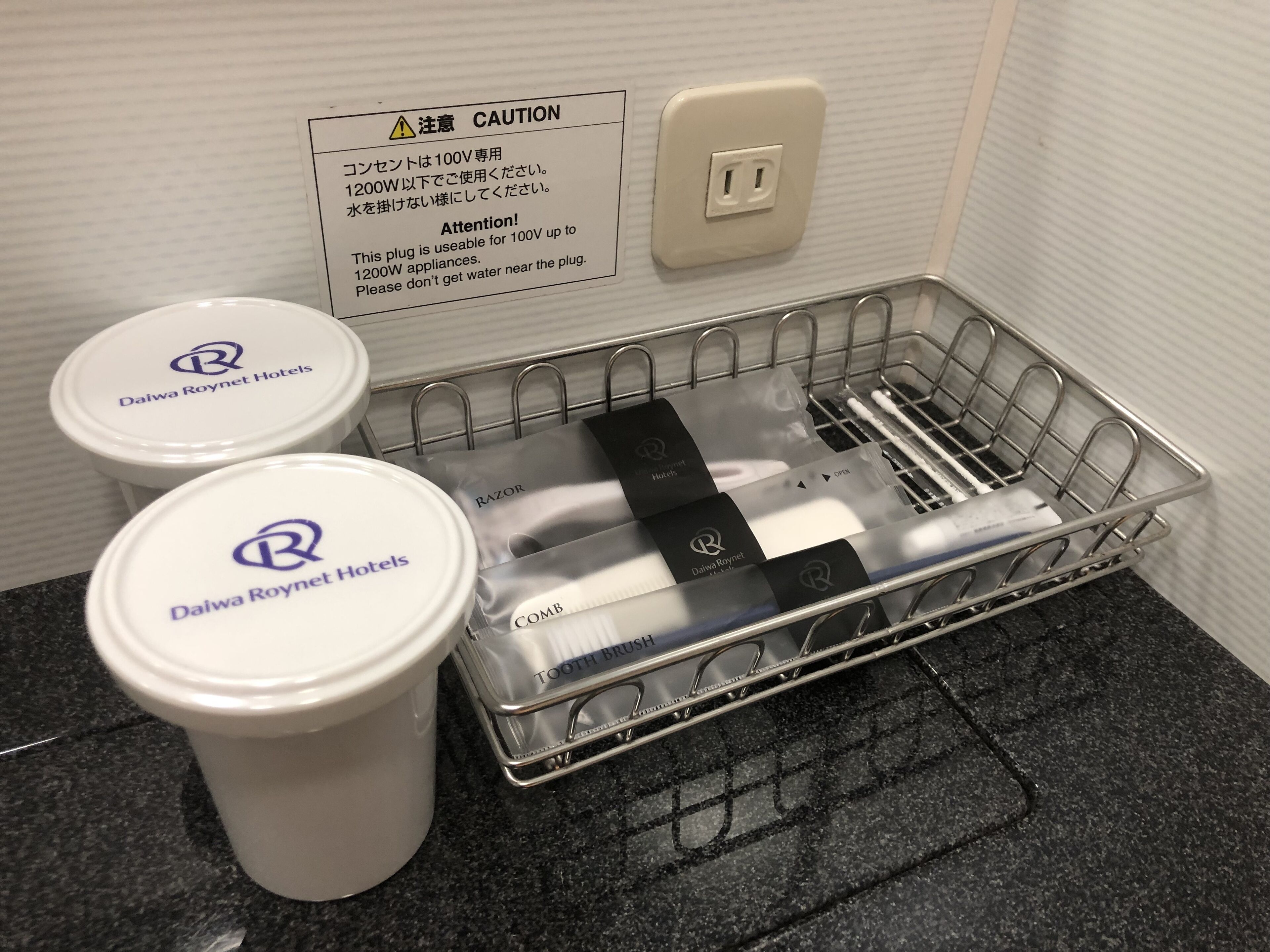 A bathroom sink area with a caution sign, a plug, and toiletries including a toothbrush and a comb.