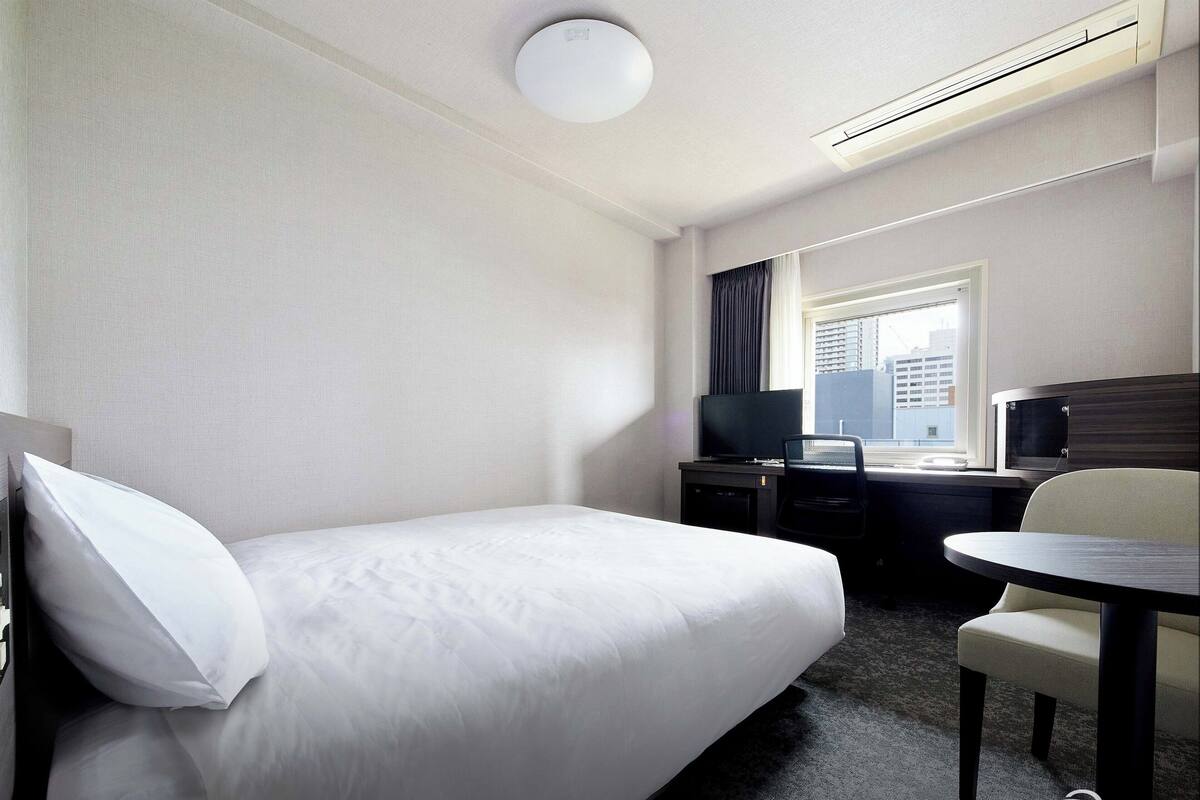 Una habitación de hotel con una cama, un escritorio con computadora, una silla y un televisor.