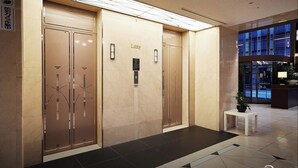 A hotel lobby with three elevators, a reception desk, and a potted plant.