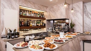 Una zona de bar con mostrador de mármol, diferentes bandejas de comida y una estantería repleta de licores.