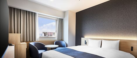 A hotel room with a large bed, a desk, two chairs, a small table, and a window with curtains.