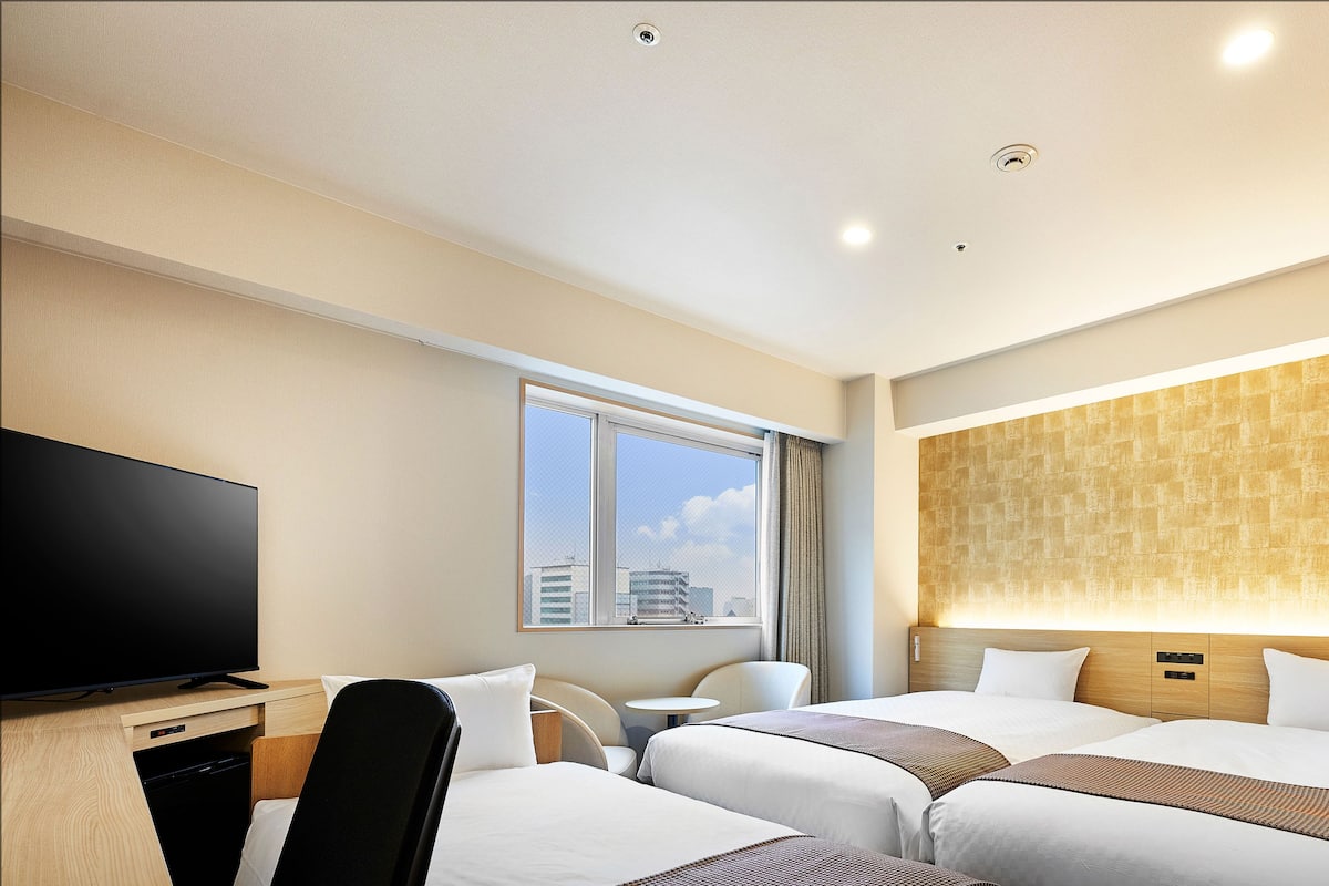Een hotelkamer met twee bedden, een bureau met een televisie, een raam met uitzicht over de stad, en een wand met een structuur.