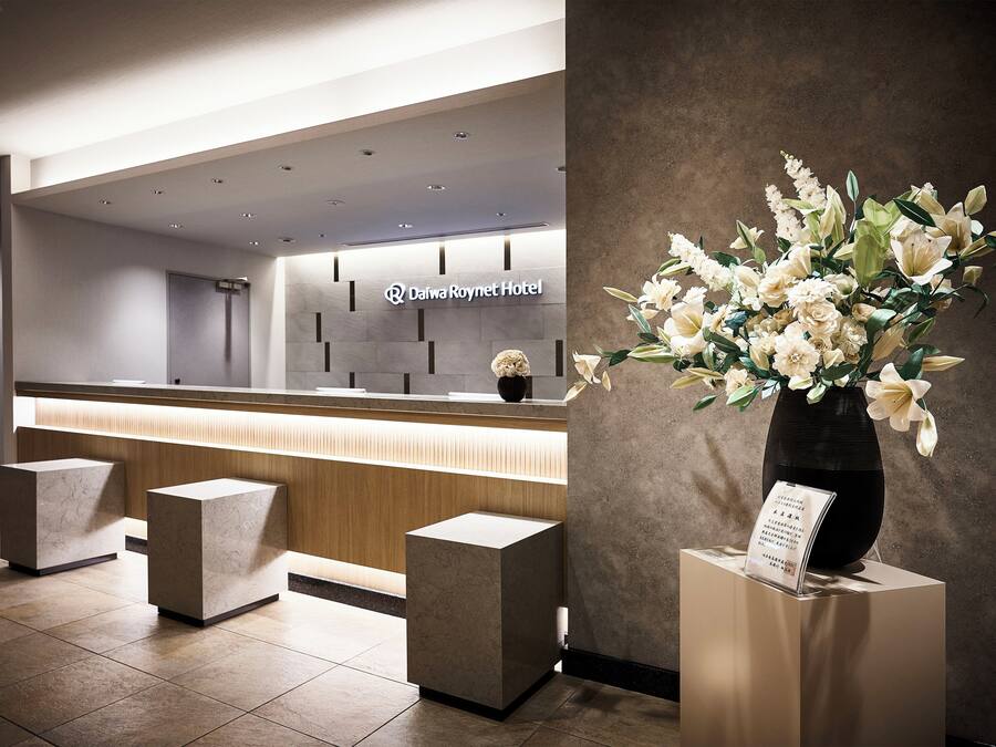 Un espace d’accueil au design moderne, comprenant un comptoir de réception, un vase de fleurs et une enseigne indiquant le nom de l’hôtel.