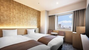 Une chambre d’hôtel avec deux lits, une petite table, un bureau et une fenêtre avec des rideaux.