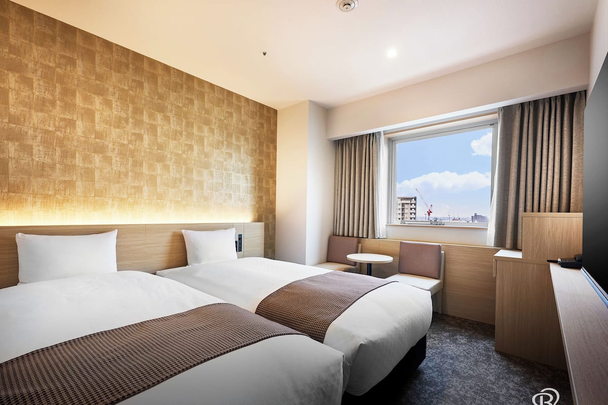 Een hotelkamer met twee bedden, een kleine tafel, een bureau en een raam met gordijnen.