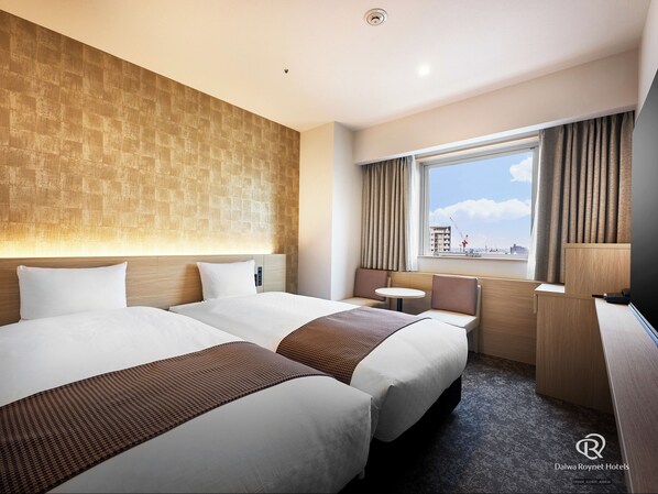 Habitación de hotel con dos camas, una mesita, un escritorio y una ventana con cortinas.